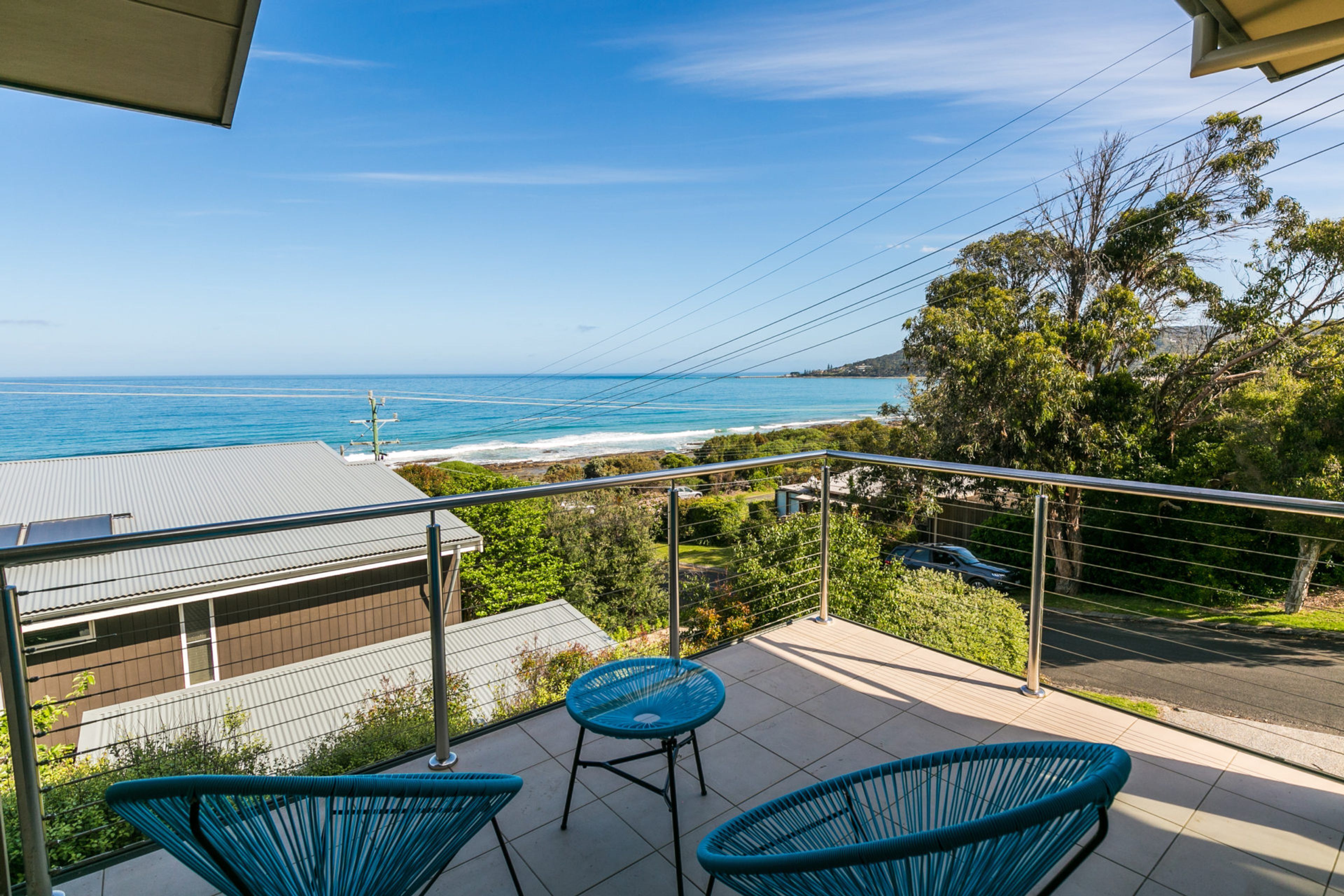 A balcony with two chairs and a table overlooking a coastal view.