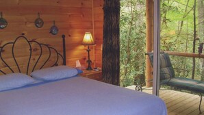 Ein Zimmer in einer Holzhütte mit einem Bett, einem Nachttisch, einer Lampe und Blick auf einen Balkon mit Sitzgelegenheit.