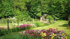 Ein Garten mit einer Holzkonstruktion, umgeben von üppigem Grün und blühenden Pflanzen.