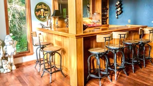 Zona de bar con mostrador de madera, taburetes y un ventanal con vistas a árboles.