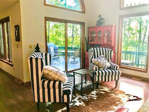 A room with striped armchairs, a glass door leading to an outdoor patio, a red cabinet, and a cowhide rug.