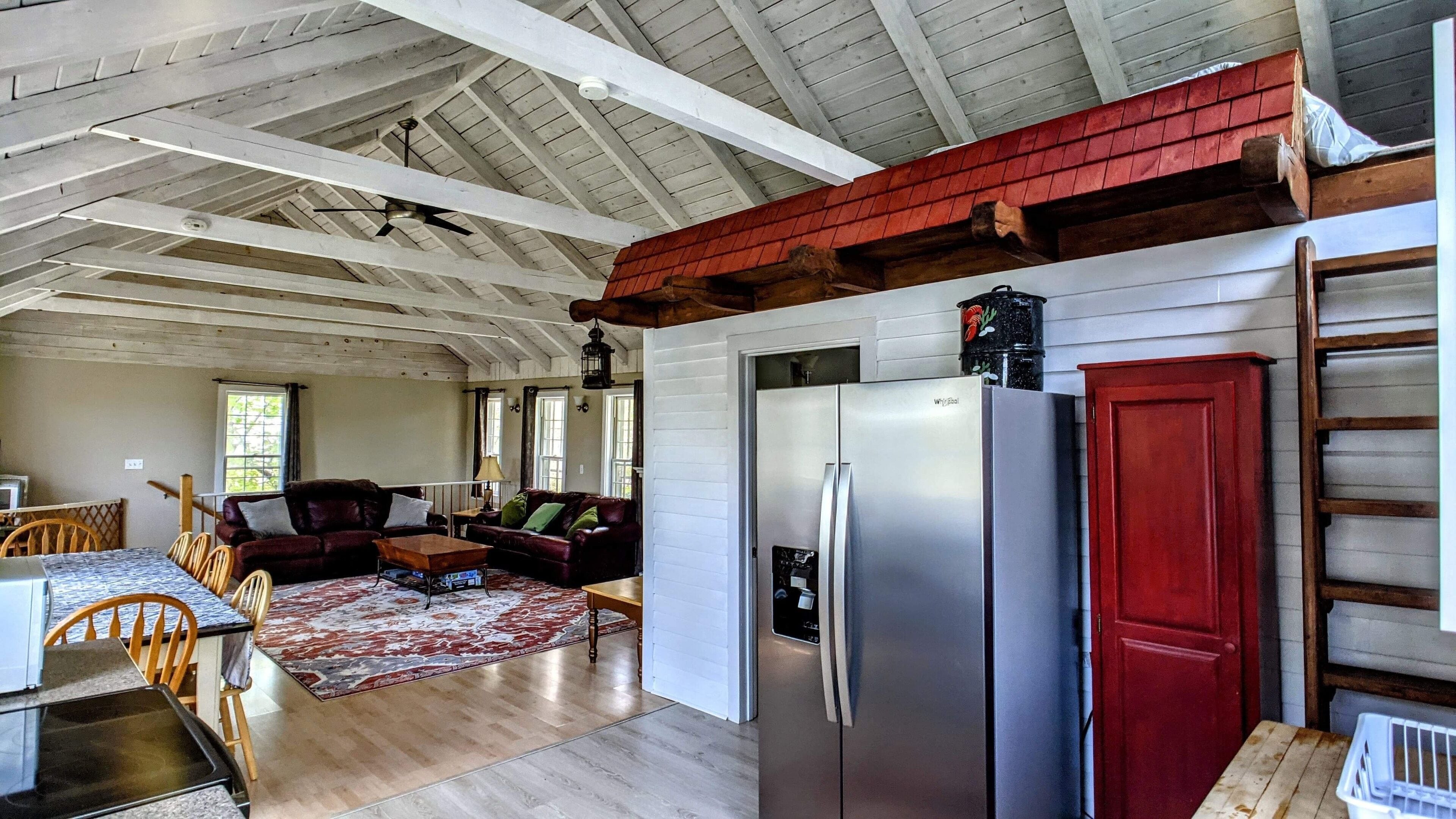 A spacious living area with a large refrigerator, wooden ceiling beams, and a dining area with a table and chairs.