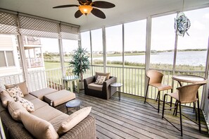 Relax in a serene outdoor space with a sofa set, chairs, and a small table, surrounded by a white lattice fence and offering views of a body of water.