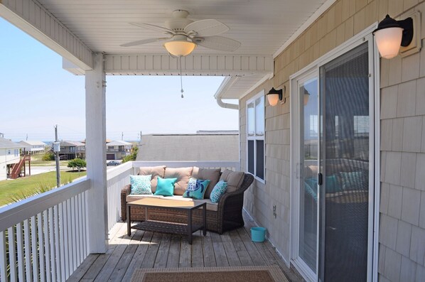 A covered porch with a ceiling fan, a cushioned seating area with pillows, and a view of the neighborhood.