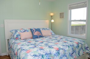 A bedroom with a bed, a nightstand, a wall-mounted lamp, and a window with a view.