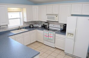 Une cuisine avec des meubles blancs, un évier, une cuisinière, un four à micro-ondes et un réfrigérateur.