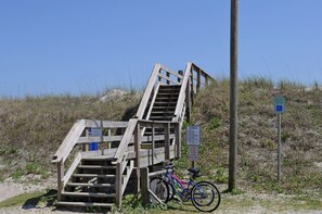 Un escalier en bois menant le long d’une pente sablonneuse, un vélo garé à proximité et un panneau indiquant une place de stationnement réservée.