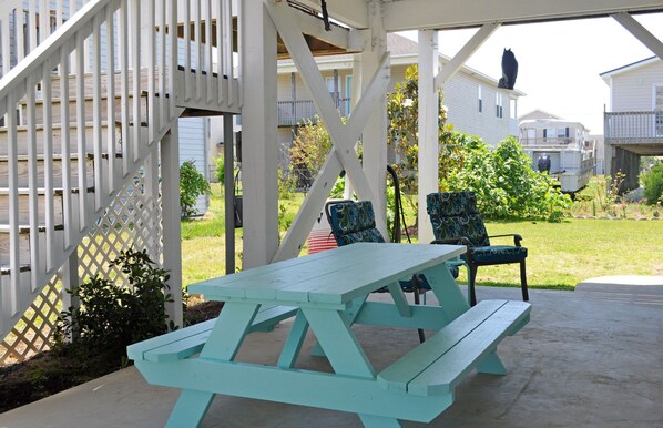 A picnic table and chairs in a covered outdoor area with a white fence and houses in the background.