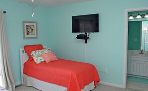 Une chambre à coucher avec un lit, un téléviseur fixé au mur et une salle de bain visible à travers une porte ouverte.