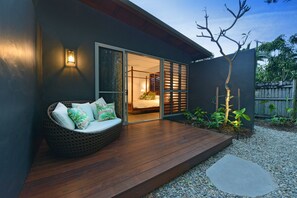A modern outdoor seating area with a wooden deck, a wicker sofa with cushions, and a small table. - The Bahama House, Luxury by the beach. (Port Douglas)