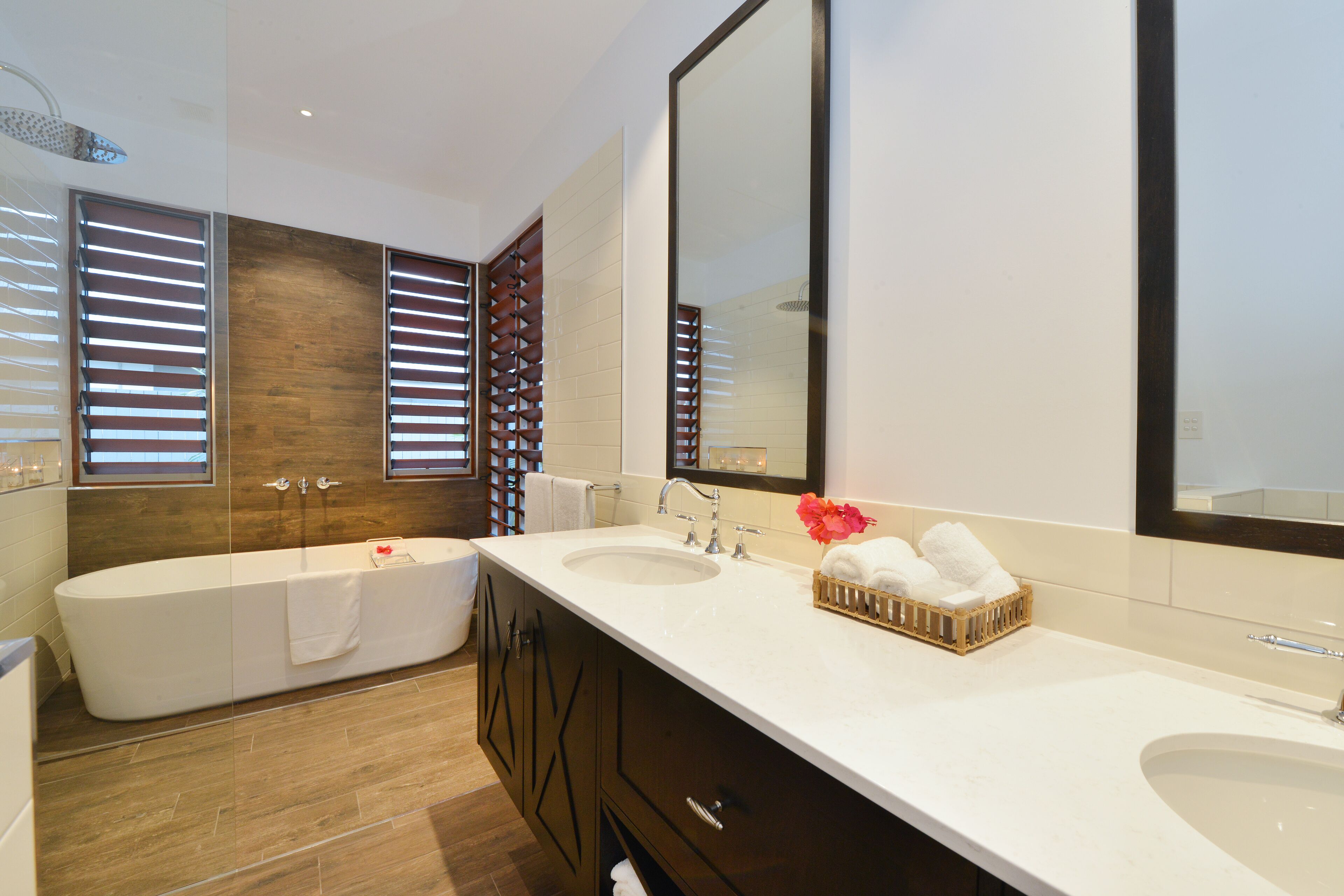 A modern bathroom with two sinks, a large mirror, and a freestanding bathtub.