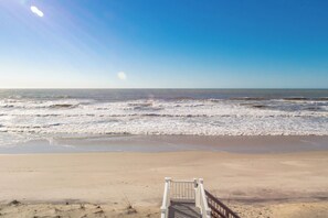 A beach with waves, a wooden walkway, and a clear sky.