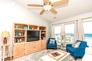 A living room with a television, bookshelves, two blue sofas, a coffee table, and a ceiling fan.