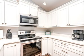 A kitchen with white cabinets, a microwave, a stove, a toaster, and a coffee maker.