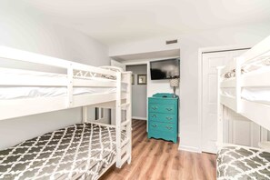 A room with bunk beds, a teal dresser, and a television on the wall.