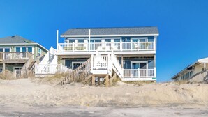 A beachfront property with a two-story building featuring a balcony, a staircase, and a flag.