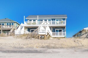 A beachfront property with a two-story building featuring a balcony, a staircase, and a flag.