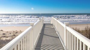 A wooden boardwalk leading to a beach with waves in the background.