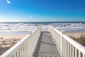 A wooden boardwalk leading to a beach with waves in the background.