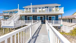 A two-story beachfront house with a covered walkway leading to the entrance.