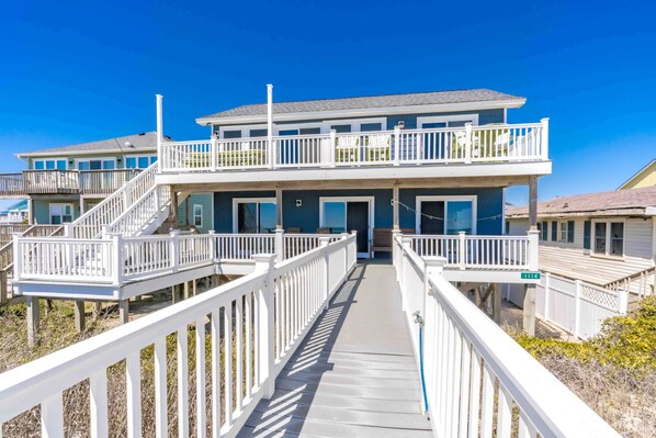 A two-story beachfront house with a covered walkway leading to the entrance.
