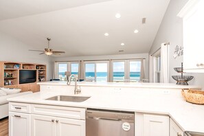 A modern kitchen with a built-in dishwasher, a large island with a sink, and a view of the ocean.