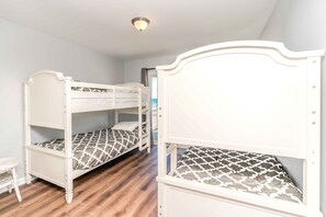A room with two bunk beds, a small table, and a view of the sea through an open door.