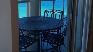 Een balkon met een ronde tafel en stoelen, met uitzicht op een heldere blauwe zee.