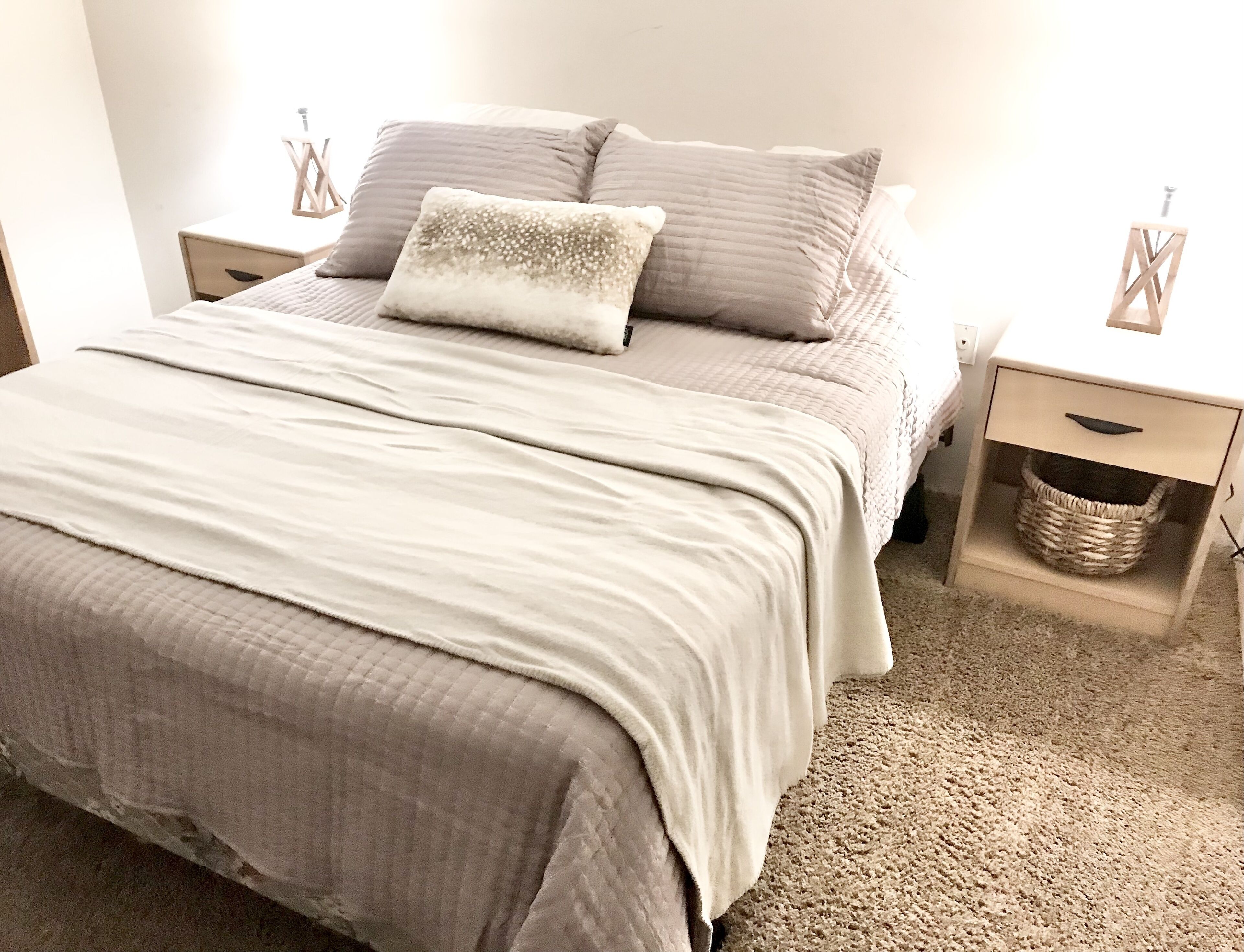 A bedroom with a bed, two nightstands, a small basket, and a wall socket.