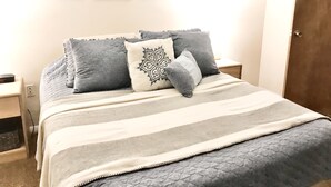 A bedroom with a bed, pillows, a bedside table, and wall art.