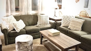 A living room with a green sofa, a wooden coffee table, and a round ottoman.