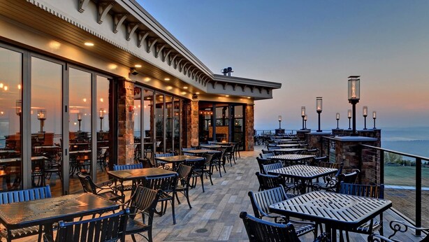 An outdoor patio with tables and chairs, a stone wall, and a view of the ocean.