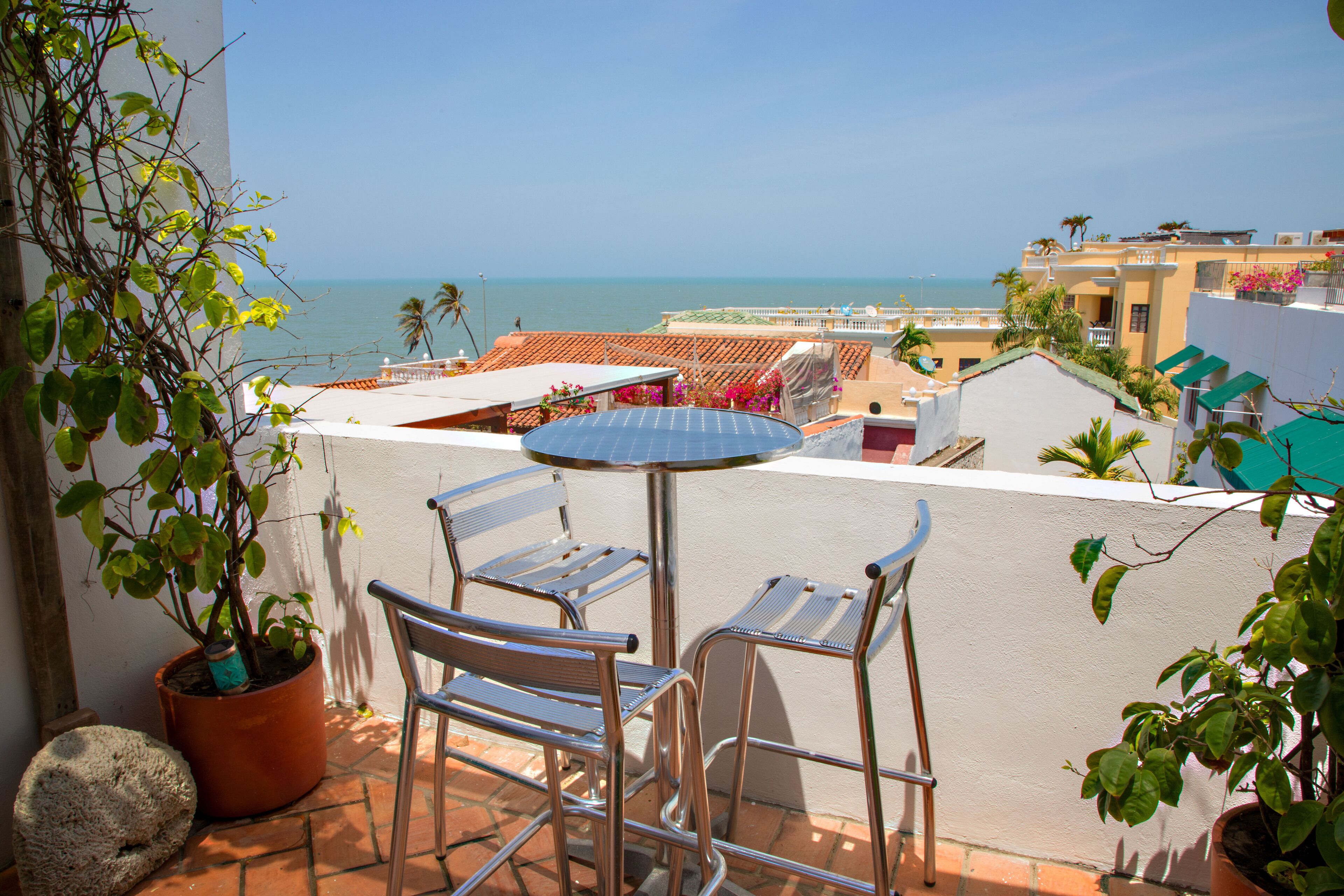 Ein Balkon mit Tisch und Stühlen, der auf eine Küstenlandschaft mit Gebäuden und dem Meer blickt.
