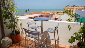 Varanda com mesa e cadeiras, vista para a costa, edifícios e o mar.