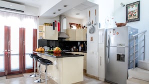 Uma cozinha moderna com uma ilha central, banquetas, geladeira e escada que leva a um andar superior.