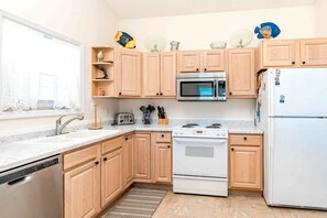 Una cocina con armarios de madera, microondas, estufa, refrigerador y pileta.