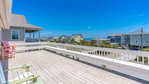 Una terraza de madera con sillas, un porche cubierto y vistas a casas y al océano.