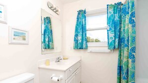 A bathroom with a toilet, sink, mirror, and window with curtains. - Flip Flops - Cozy 2nd Row Home - Ocean Views! (Surf City)