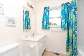 A bathroom with a toilet, sink, mirror, and window with curtains. - Flip Flops - Cozy 2nd Row Home - Ocean Views! (Surf City)