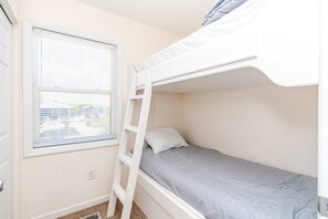 A bunk bed with a ladder, a window with blinds, and a door. - Flip Flops - Cozy 2nd Row Home - Ocean Views! (Surf City)
