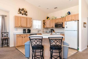 A kitchen with wooden cabinets, a central island with chairs, a microwave, a refrigerator, and a coffee maker. - Flip Flops - Cozy 2nd Row Home - Ocean Views! (Surf City)