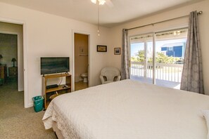A bedroom with a large bed, a television on a stand, a chair, and a balcony with a view. - Flip Flops - Cozy 2nd Row Home - Ocean Views! (Surf City)