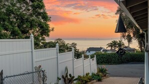 A residential area with a white fence, a cactus plant, and a view of the ocean at sunset. - MAGICAL 5-STAR RATED OCEAN VIEW CUSTOM HOME - PLEASE READ ALL 400 GUEST REVIEWS! (Summerland)