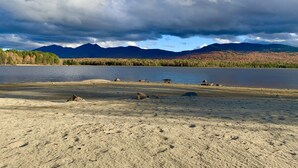 Vista sul lago con montagne sullo sfondo e una spiaggia sabbiosa in primo piano.