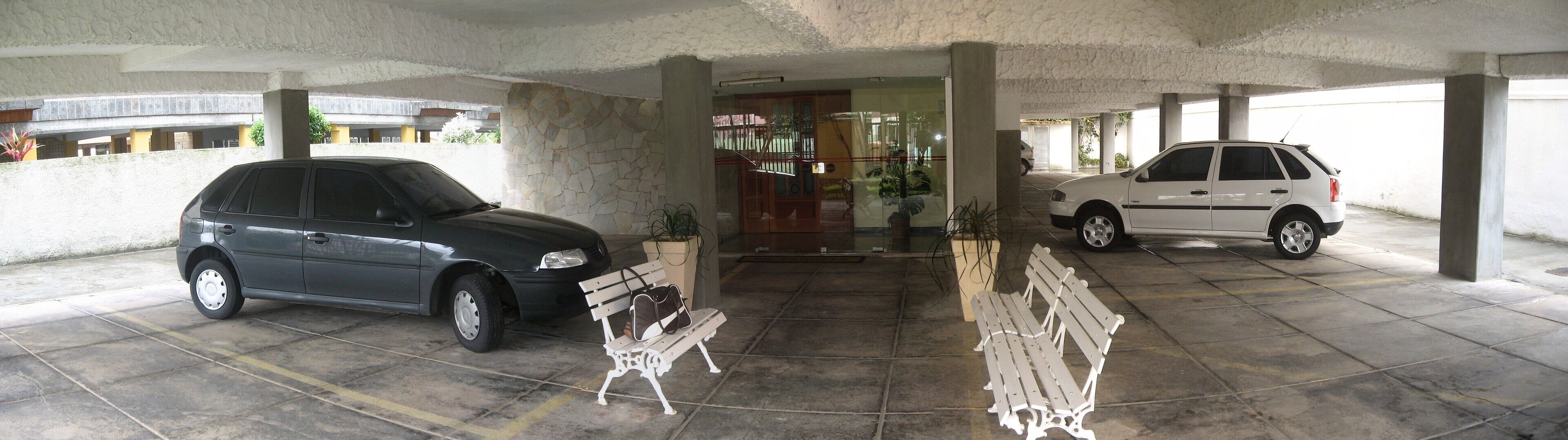 A covered parking area with two cars parked, a bench, and a door leading to a building.