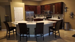 A modern kitchen with a central island, dark wood cabinets, stainless steel appliances, and a tiled floor.