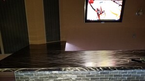 A room with a black marble floor, a brick-patterned accent wall, and a television mounted on the wall displaying a basketball game.