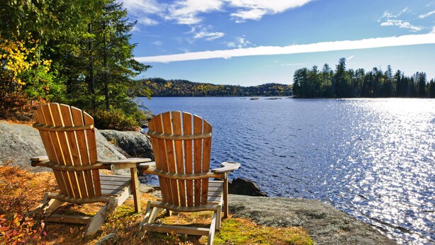 Deux fauteuils Adirondack sont placés face à un lac, dont les rives sont bordées d’une forêt.