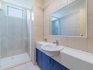 Ein modernes Badezimmer mit einer Duschkabine aus Glas, einem weißen Waschbecken und einem großen Spiegel darüber.