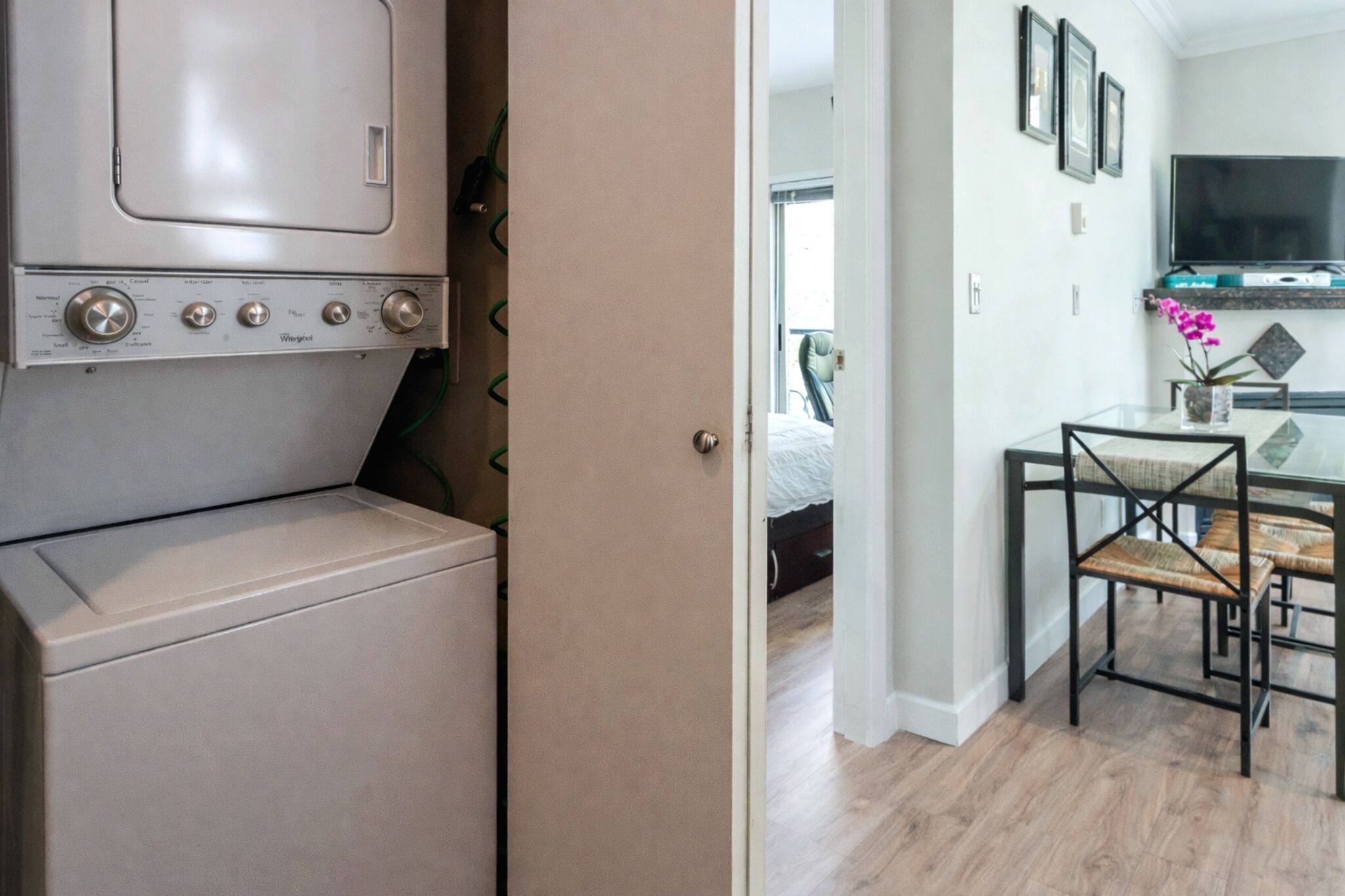 A laundry area with a washing machine, a dining area with a table and chairs, and a television mounted on the wall.